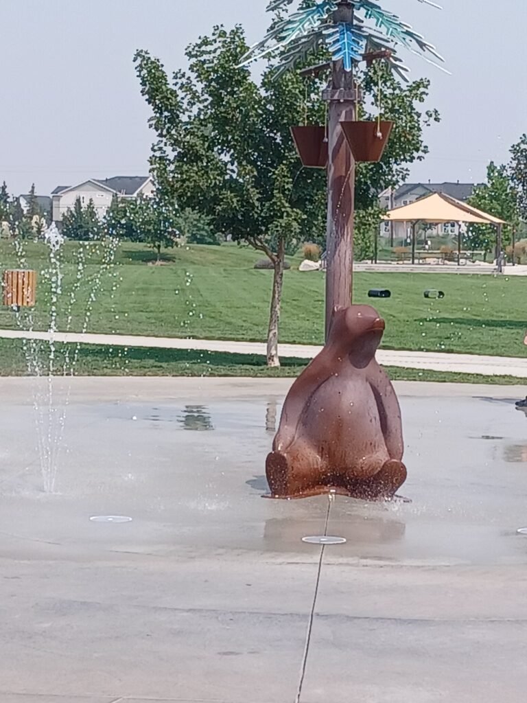 Bear-themed splash pad at Discovery Park in Meridian, Idaho, featuring interactive water sprays, ground fountains, and shaded park areas.
