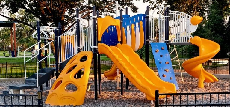 Bright yellow and blue playground beneath large shade trees in an Idaho park